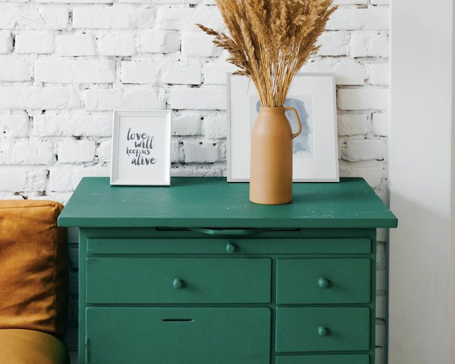 photo of a green dresser, with a vase and picture frame on top, with a brown sofa on the left.