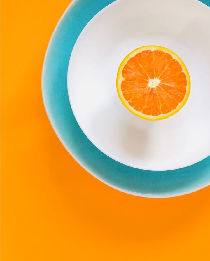 blue bowl, top view with a white liquid and an orange slice in the center on a yellow background